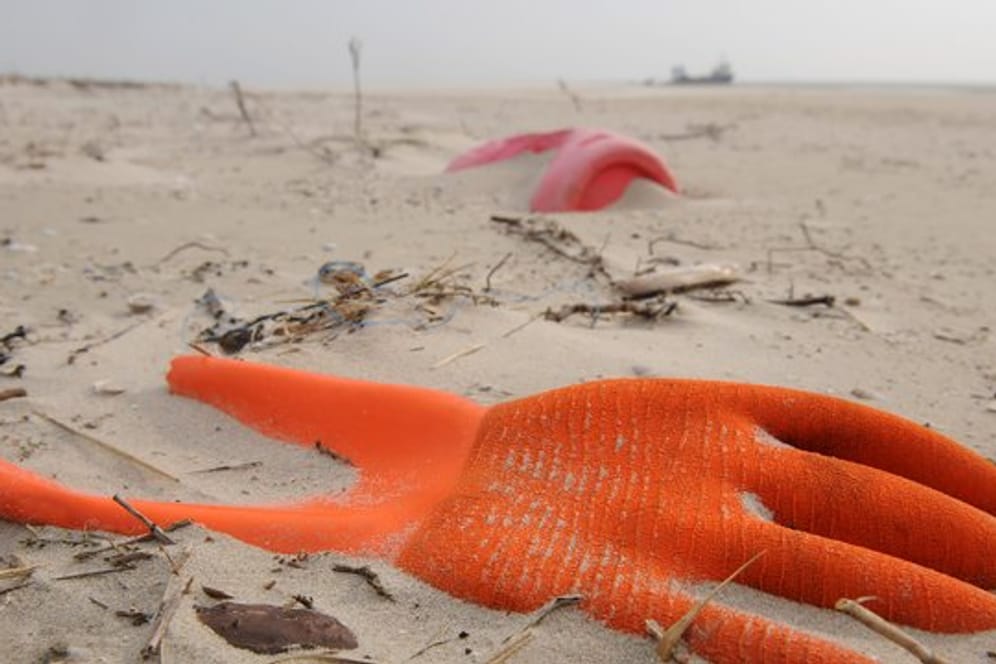 Angespülter Unrat in Form eines Arbeitshandschuhs und eines Kunststoffkanisters am Strand der Vogelschutzinsel Memmert, Niedersachsen.