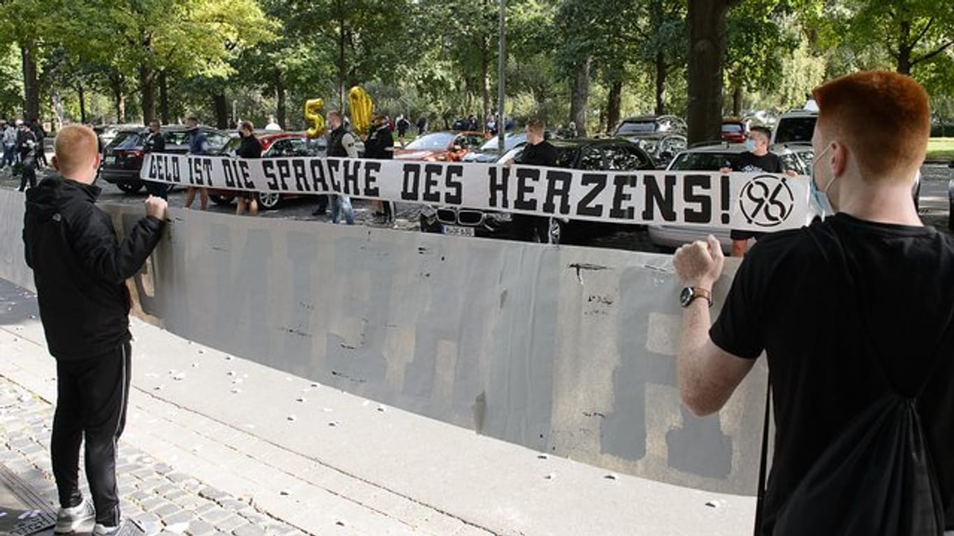 Fans von Hannover 96 stehen mit einem Banner "Geld ist die Sprache des Herzens" am VIP-Eingang des Stadions vor dem Spiel Spalier.