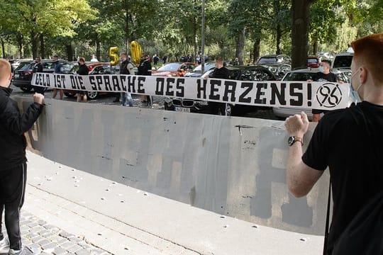 Fans von Hannover 96 stehen mit einem Banner "Geld ist die Sprache des Herzens" am VIP-Eingang des Stadions vor dem Spiel Spalier.