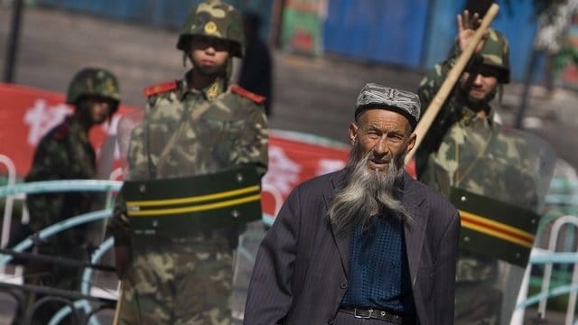 Ein Angehöriger der uigurischen Minderheit in der Unruheregion Xinjiang in Nordwestchina geht vorbei an chinesischen Sicherheitskräften. Ein Angehöriger der uigurischen Minderheit in der Unruheregion Xinjiang in Nordwestchina geht vorbei an chinesischen Sicherheitskräften.