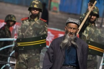 Ein Angehöriger der uigurischen Minderheit in der Unruheregion Xinjiang in Nordwestchina geht vorbei an chinesischen Sicherheitskräften.