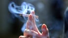 Eine Hand hält eine brennende Zigarette (Archivbild): Rauchen während der Arbeitszeit ist oft möglich, das Recht sieht aber auch Einschränkungen vor.