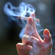 Eine Hand hält eine brennende Zigarette (Archivbild): Rauchen während der Arbeitszeit ist oft möglich, das Recht sieht aber auch Einschränkungen vor.