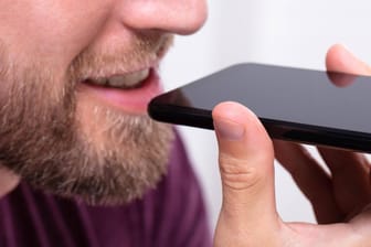 Ein Mann spricht in sein Smartphone-Mikrofon: Wenn der Google Assistant nicht mehr lauschen soll, gibt es mehrere Möglichkeiten, ihn abzustellen.