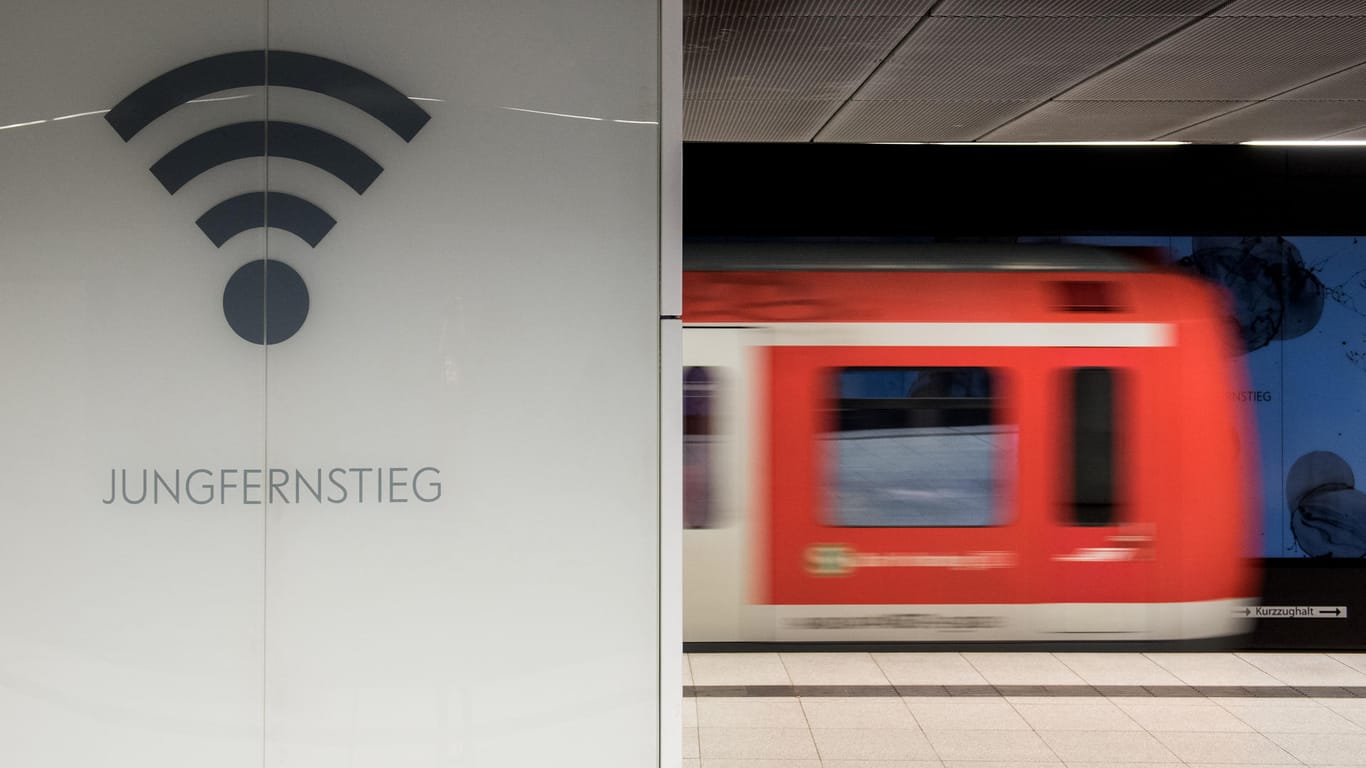 Eine S-Bahn fährt im Bahnhof Jungfernstieg hinter einem Schild mit dem Symbol für "WLAN".