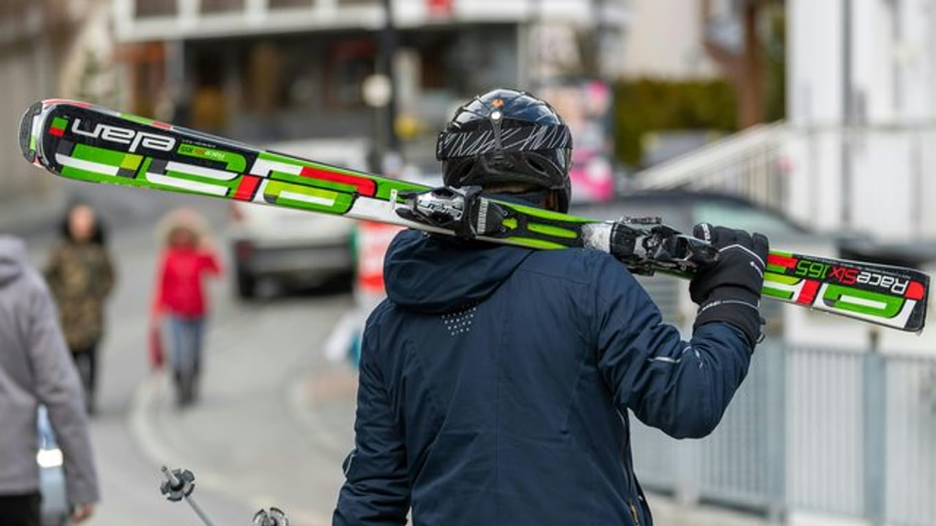 Ein Skifahrer geht mit geschulterten Skiern auf einer Straße im Skiort Ischgl.