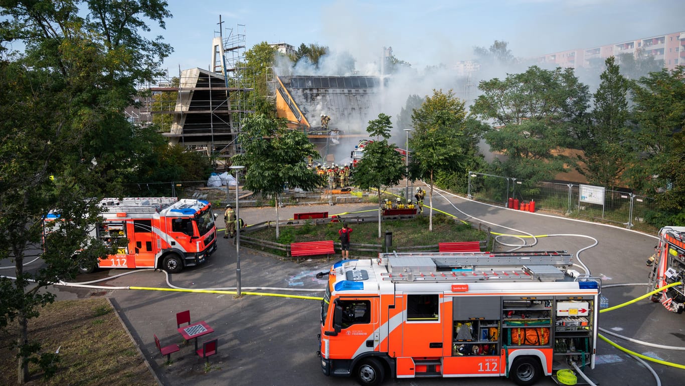 Zahlreiche Feuerwehrleute und einige Löschwagen der Feuerwehr: Sie stehen während der Löscharbeiten vor der brennenden Jeremia-Kirche in Berlin-Spandau.