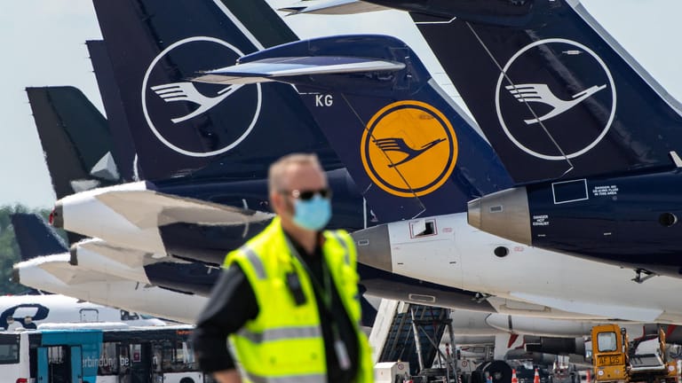 Ein Mann mit Mundschutz vor Lufthansa-Maschinen (Symbolbild): Die Airline verschärft ihren Sparkurs.
