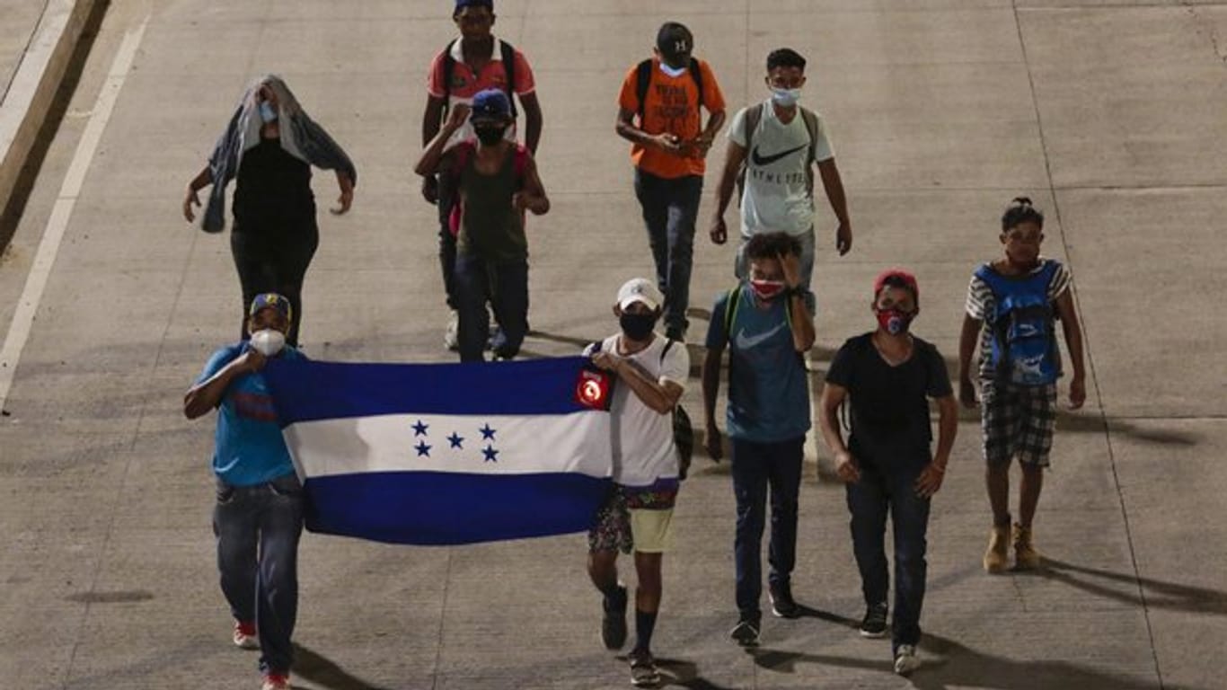 Menschen tragen eine Fahne von Honduras und gehen in der Hoffnung, zukünftig die USA zu erreichen, einen Highway entlang.