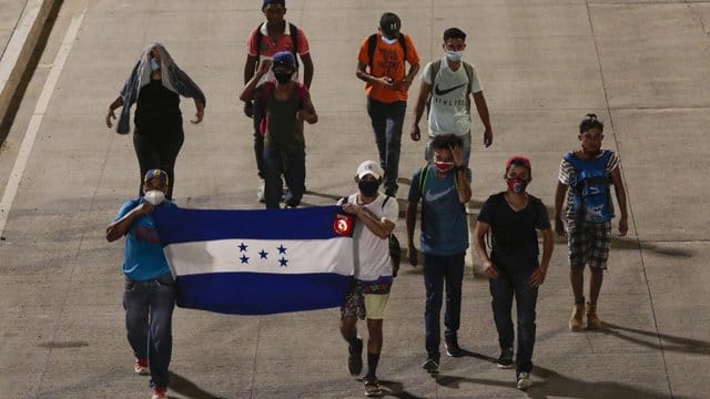 Menschen tragen eine Fahne von Honduras und gehen in der Hoffnung, zukünftig die USA zu erreichen, einen Highway entlang. Menschen tragen eine Fahne von Honduras und gehen in der Hoffnung, zukünftig die USA zu erreichen, einen Highway entlang.