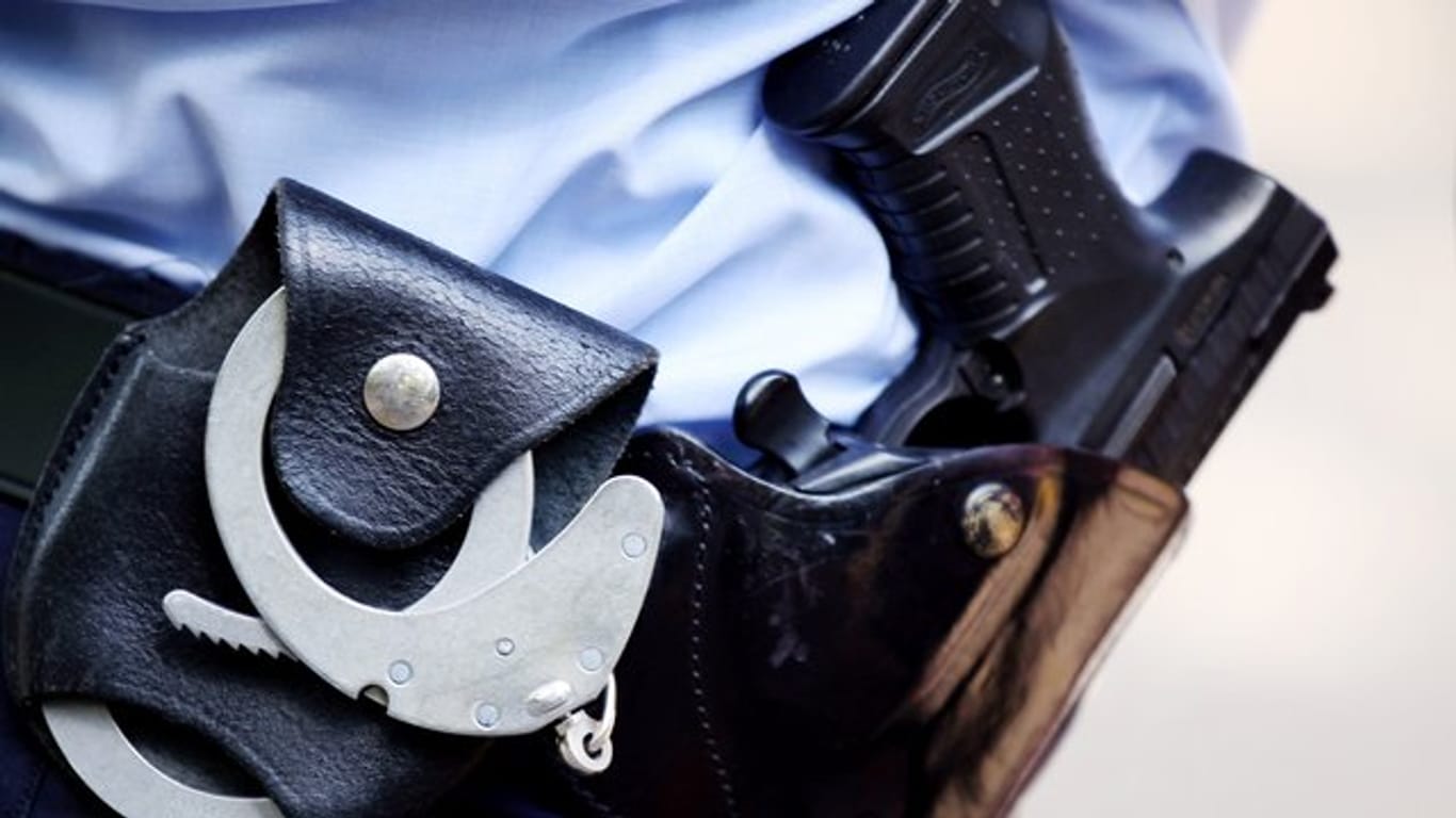 Ein Polizist mit Handschellen und Pistole (Symbolbild): In Köln hat sich ein Mann einer Kontrolle entziehen wollen.