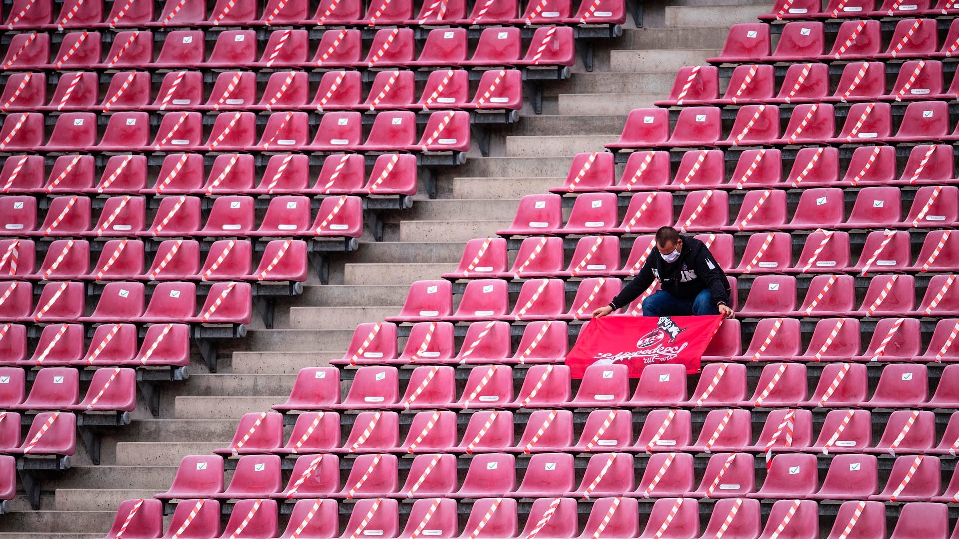 Ein Mann platziert vor der Partie eine Köln-Fahne auf den Sitzplätzen vor ihm: Ins Stadion durften zum Rheinderby nur einige Hundert Fans.