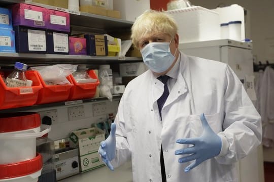 Boris Johnson, Premierminister von Großbritannien, gestikuliert mit seinen Händen und trägt Schutzkleidung und Maske.