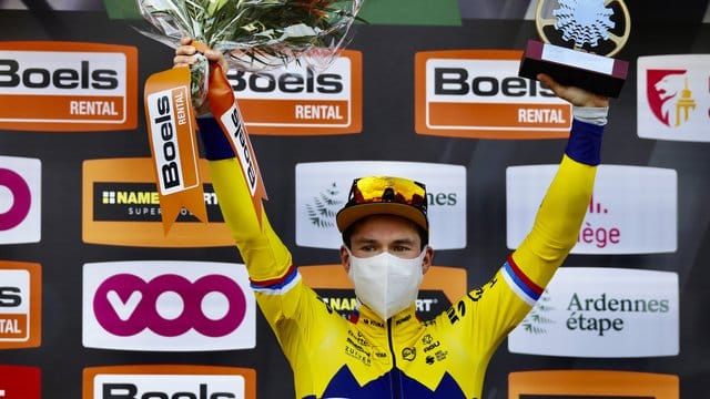 Der Slowene Primoz Roglic vom Team Jumbo jubelt mit Mund-Nasen-Schutz und Pokal bei der Siegerehrung auf dem Podium.