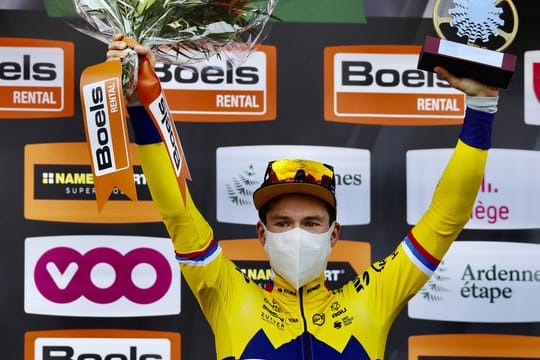 Der Slowene Primoz Roglic vom Team Jumbo jubelt mit Mund-Nasen-Schutz und Pokal bei der Siegerehrung auf dem Podium.