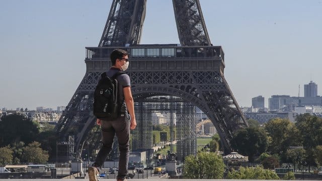 Ein Passant geht mit Mundschutzmaske über den Place du Trocadéro, während im Hintergrund ein Teil des Eiffelturms zu sehen ist.