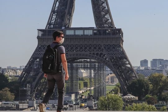 Ein Passant geht mit Mundschutzmaske über den Place du Trocadéro, während im Hintergrund ein Teil des Eiffelturms zu sehen ist.