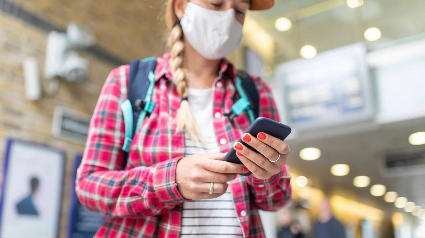 Eine Bahnreisende blickt auf ihr Smartphone: Wie gefährlich sind Zugfahrten in Zeiten der Coronavirus-Pandemie? Ein Online-Rechner erlaubt eine Schätzung des Risikos.