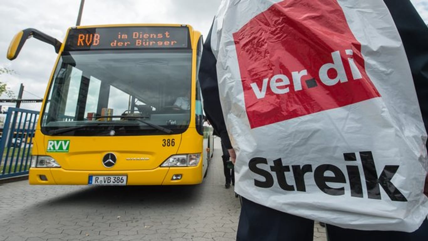 Ein streikender Busfahrer steht in Regensburg vor einem Bus.