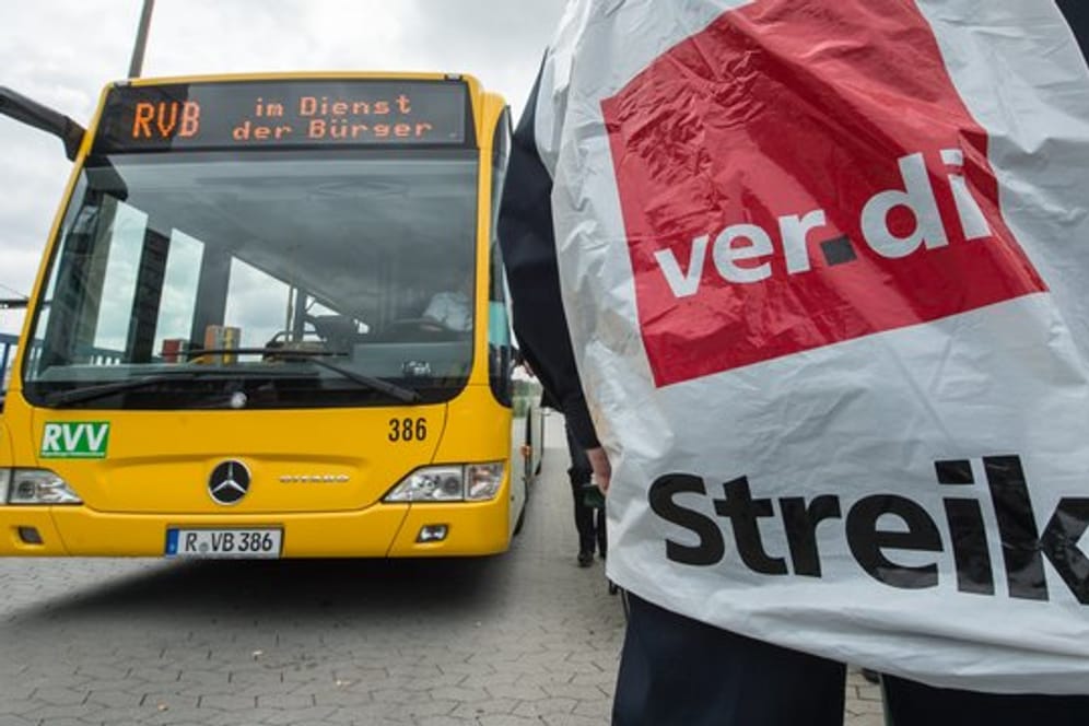 Ein streikender Busfahrer steht in Regensburg vor einem Bus.