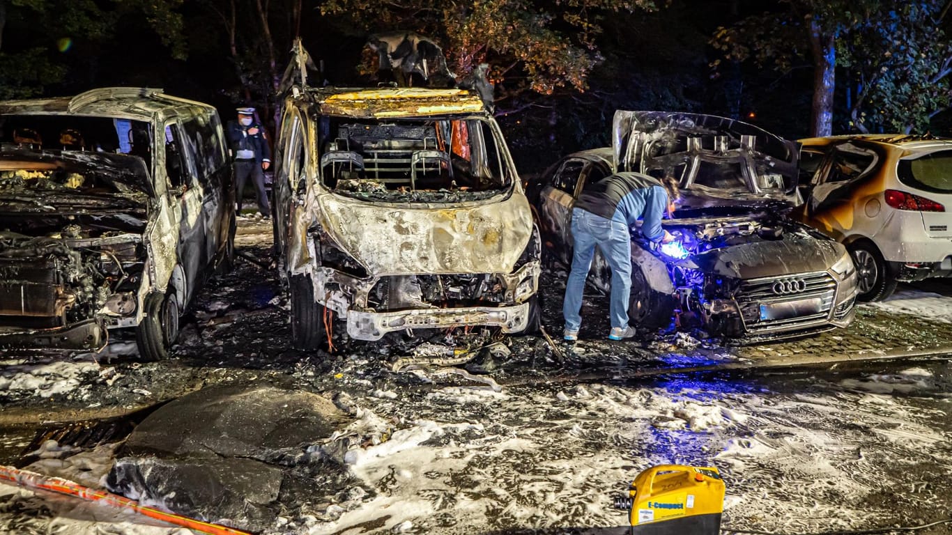 Polizisten stehen um verbrannte Fahrzeuge herum, Löschschaum liegt auf dem Boden: Nach dem Brand mehrerer Fahrzeuge in Stuttgart ermittelt die Polizei.
