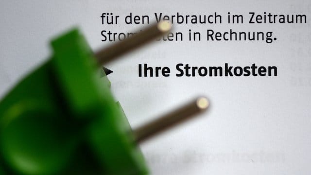 Ein grüner Stromstecker liegt auf einer Stromrechnung