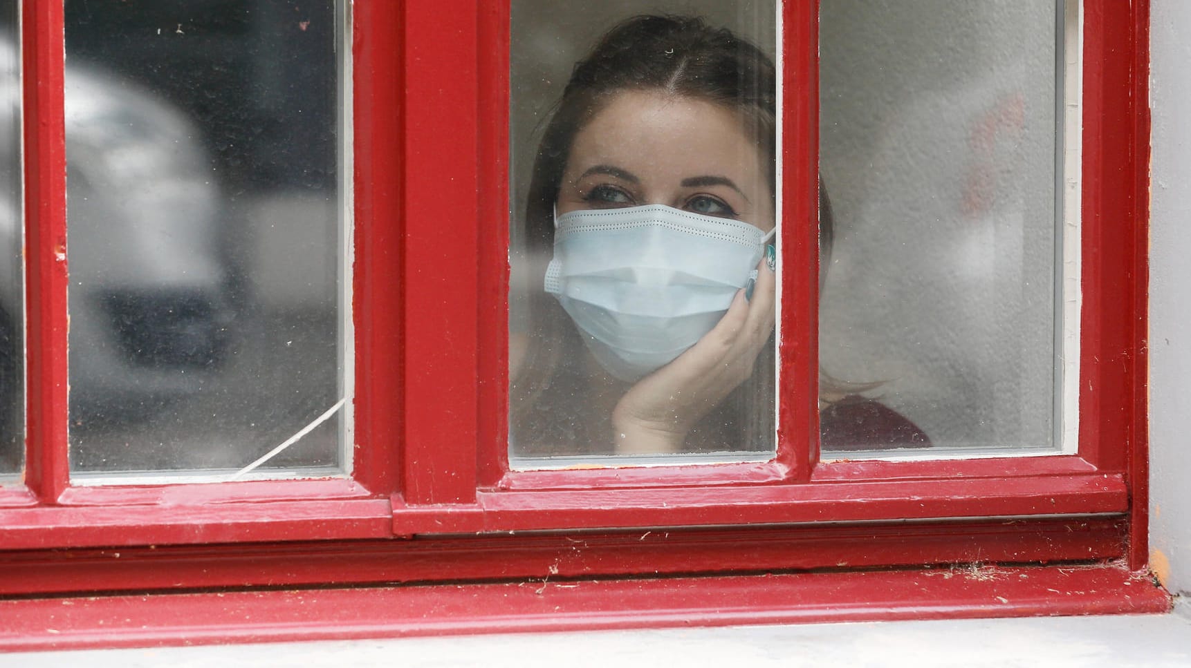 Eine Frau mit Maske blickt aus dem Fenster (Symbolbild): Wie Sie den Corona-Herbst gut überstehen, erfahren Sie im Artikel.