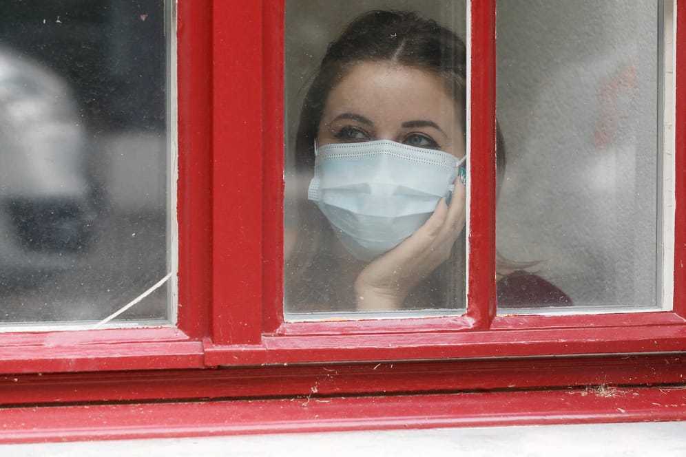 Eine Frau mit Maske blickt aus dem Fenster (Symbolbild): Wie Sie den Corona-Herbst gut überstehen, erfahren Sie im Artikel.