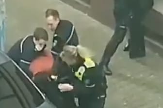 Zwei Polizisten halten den Mann fest, während ihre Kollegin auf den Festgenommenen einboxt: Der Vorfall soll nun geprüft werden.