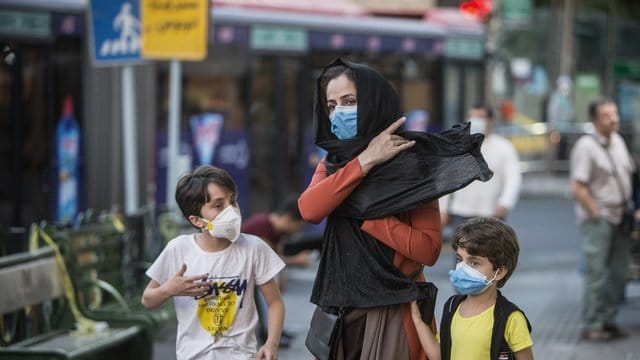 Kinder mit Gesichtsmasken gehen mit ihrer Mutter eine Straße entlang in Teheran. Kinder mit Gesichtsmasken gehen mit ihrer Mutter eine Straße entlang in Teheran.