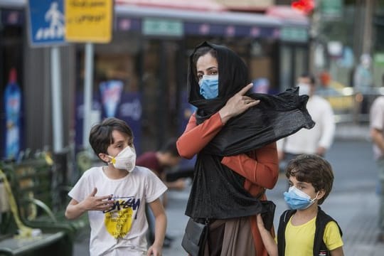 Kinder mit Gesichtsmasken gehen mit ihrer Mutter eine Straße entlang in Teheran.