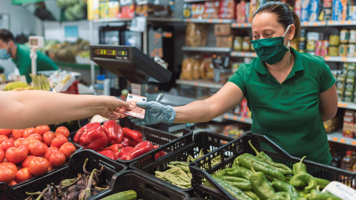 Eine Frau nimmt Geld an einer Gemüsetheke entgegen (Symboldbild): In Köln eröffnet ein Supermarkt mit "Mitmach-Konzept".
