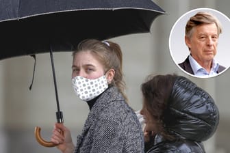 Eine Frau mit Mund-Nasen-Schutz unter einem Regenschirm: Nicht nur das Herbstwetter drückt auf die Laune, auch die unübersichtliche Regelflut sorgt für Unmut. (Symbolbild)