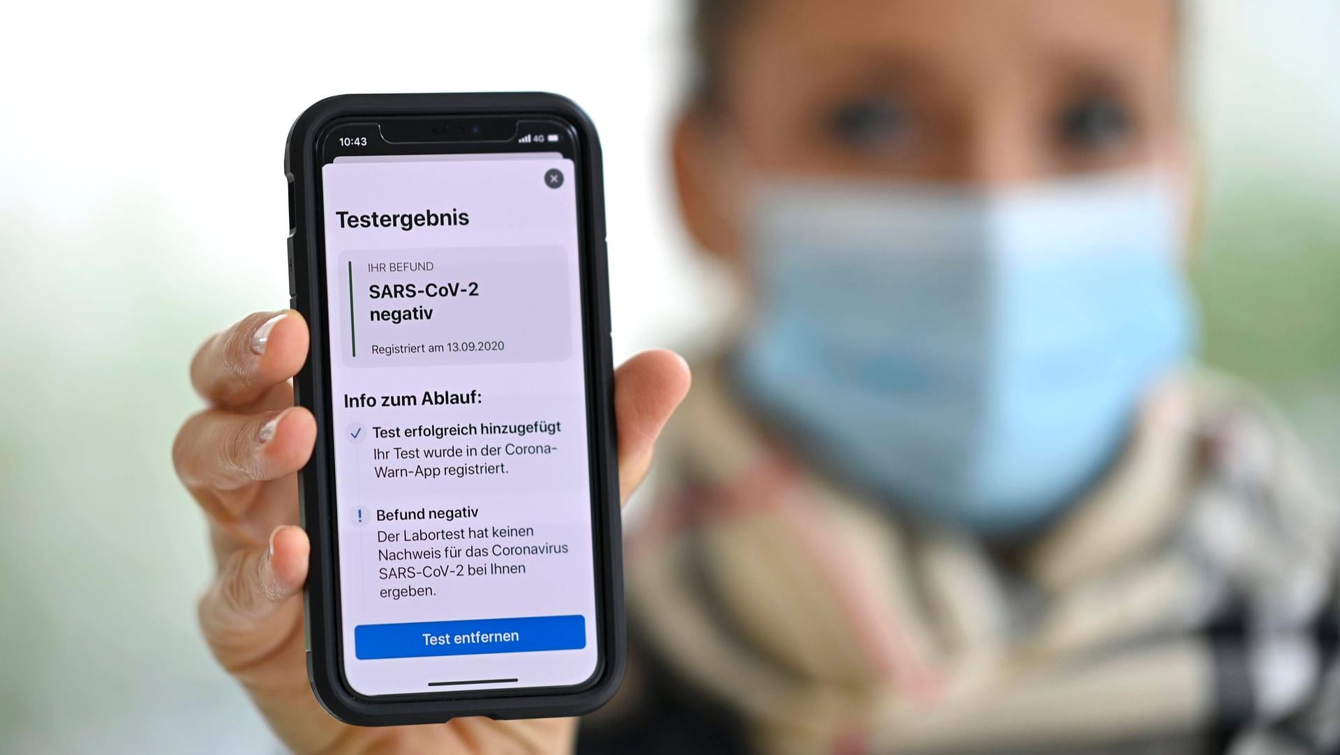 Frau mit Mundschutzmaske und Smartphone: Sie zeigt auf ihrem Handy mit der Corona Warn-APP ein negatives Testergebnis.