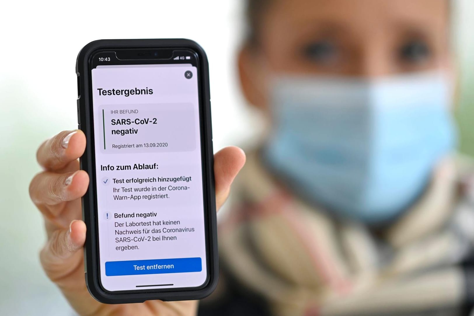 Frau mit Mundschutzmaske und Smartphone: Sie zeigt auf ihrem Handy mit der Corona Warn-APP ein negatives Testergebnis.