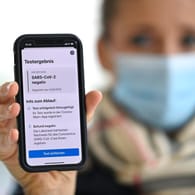 Frau mit Mundschutzmaske und Smartphone: Sie zeigt auf ihrem Handy mit der Corona Warn-APP ein negatives Testergebnis.