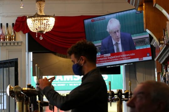 Ein Mitarbeiter eines Liverpooler Pubs schenkt Bier ein, während Premierminister Johnson im Hintergrund das neue Drei-Stufen-System erklärt.