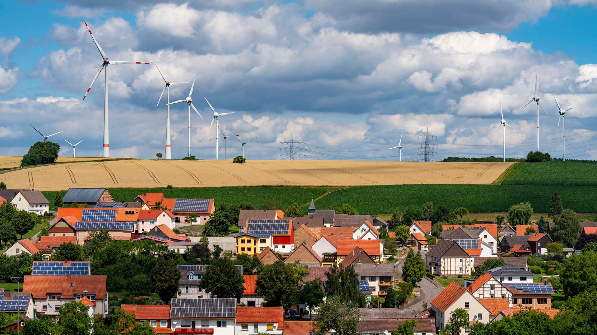 Photovoltaik-Anlagen auf Hausdächern, Windkraftwerke am Horizont: Erneuerbare Energien sind unverzichtbar für Klimaneutralität.