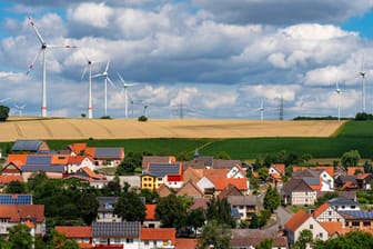 Photovoltaik-Anlagen auf Hausdächern, Windkraftwerke am Horizont: Erneuerbare Energien sind unverzichtbar für Klimaneutralität.
