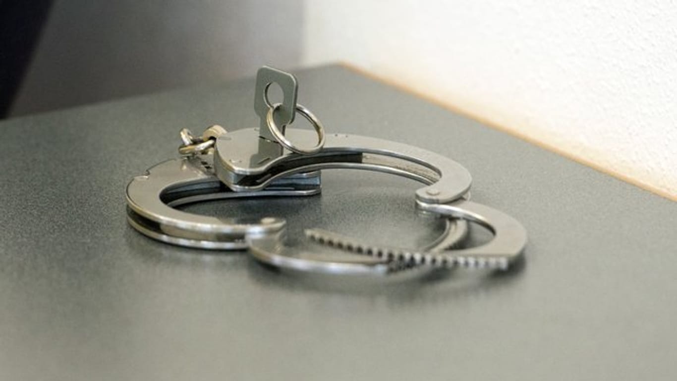 Handschellen liegen auf einem Tisch (Symbolbild): In Nürnberg soll ein Mann seine Ehefrau getötet haben, schweigt aber zu den Tatvorwürfen.
