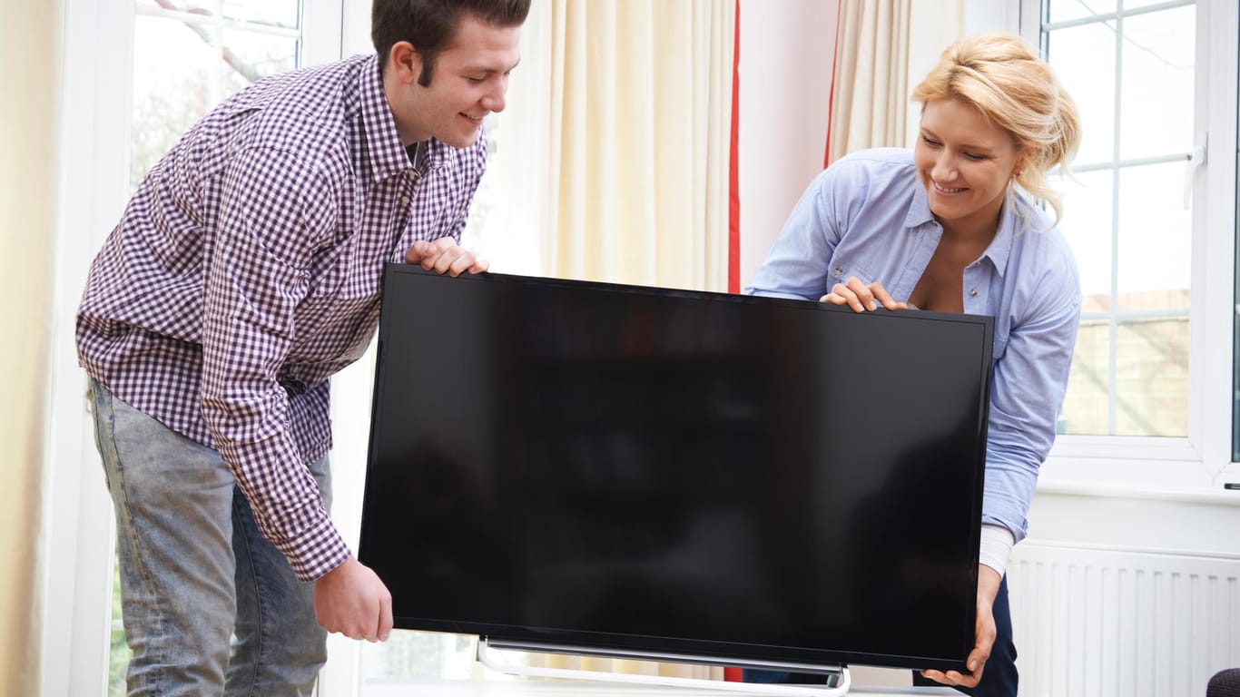 Ein Pärchen stellt einen neuen Fernseher auf: Viele Deutsche leisten sich 2020 einen neuen Fernseher.