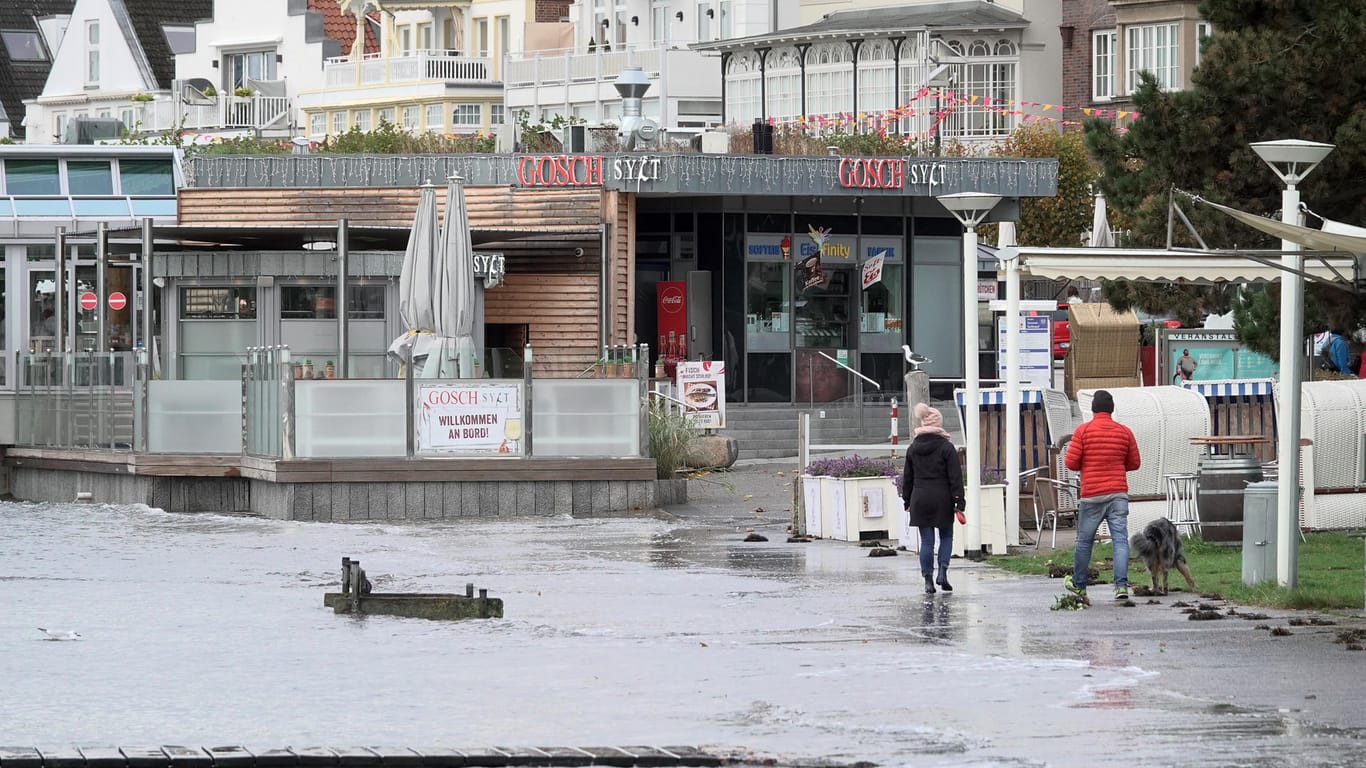 Travemünde: Passanten gehen an der Strandpromenade entlang, die bereits zu Teilen überflutet ist.