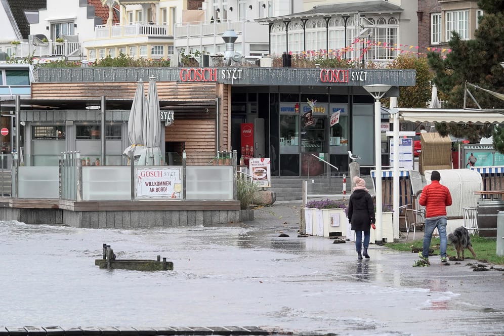 Travemünde: Passanten gehen an der Strandpromenade entlang, die bereits zu Teilen überflutet ist.