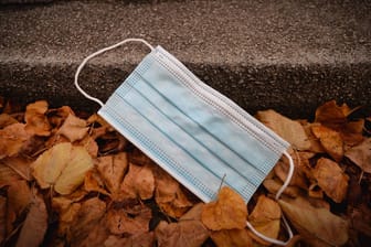 Weggeworfene Mundschutzmaske liegt am Boden im Herbstlaub.