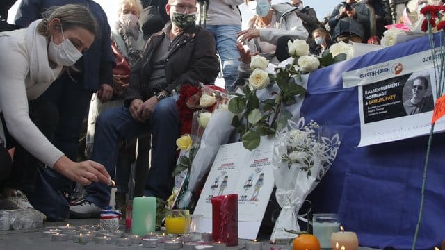 Eine Frau zündet eine Kerze an: Zahlreiche Menschen haben sich nach der brutalen Ermordung eines Lehrers am Wochenende zu einer Solidaritätsdemonstration in Paris versammelt. Eine Frau zündet eine Kerze an: Zahlreiche Menschen haben sich nach der brutalen Ermordung eines Lehrers am Wochenende zu einer Solidaritätsdemonstration in Paris versammelt.