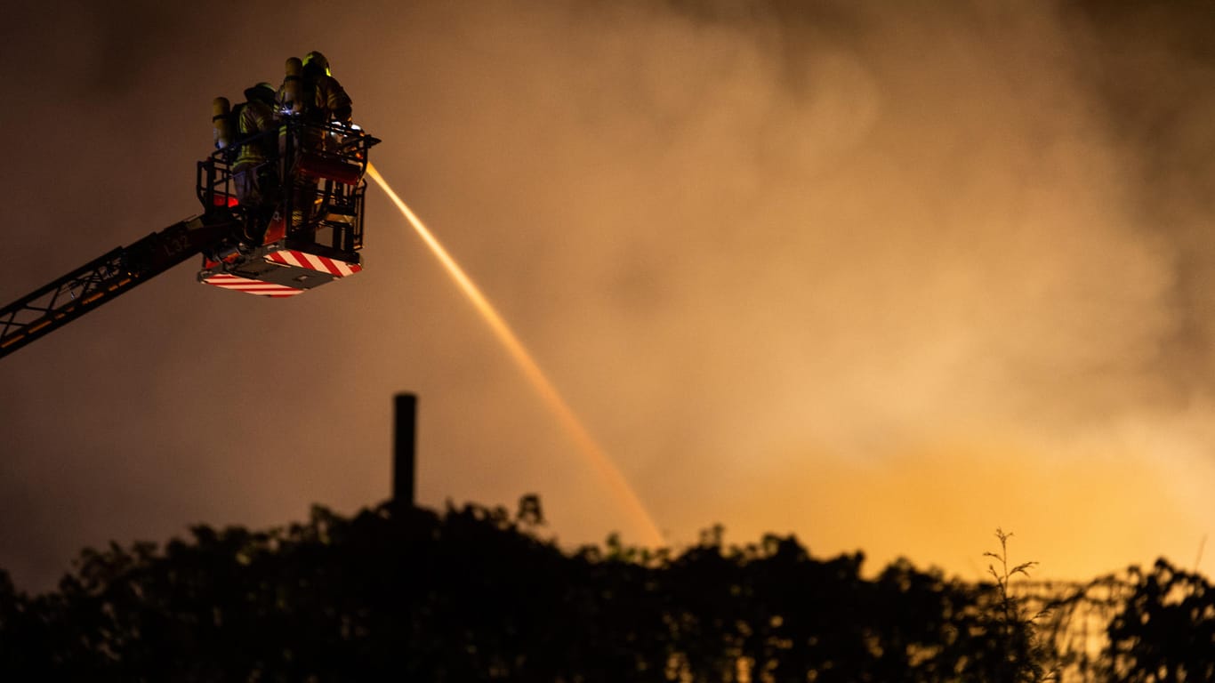 Feuerwehrleute auf einer Leiter löschen von oben eine brennende Halle: Eine 500 Quadratmeter große Lagerhalle in Berlin-Gesundbrunnen ist vollständig in Brand geraten.