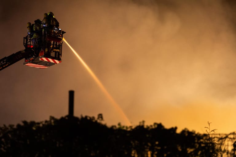 Feuerwehrleute auf einer Leiter löschen von oben eine brennende Halle: Eine 500 Quadratmeter große Lagerhalle in Berlin-Gesundbrunnen ist vollständig in Brand geraten.