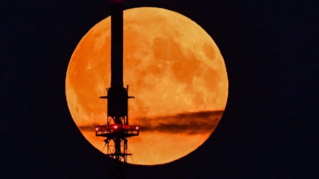 Der rötlich schimmernde Vollmond leuchtet hinter einem Funkmast.