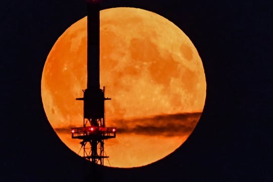 Der rötlich schimmernde Vollmond leuchtet hinter einem Funkmast.