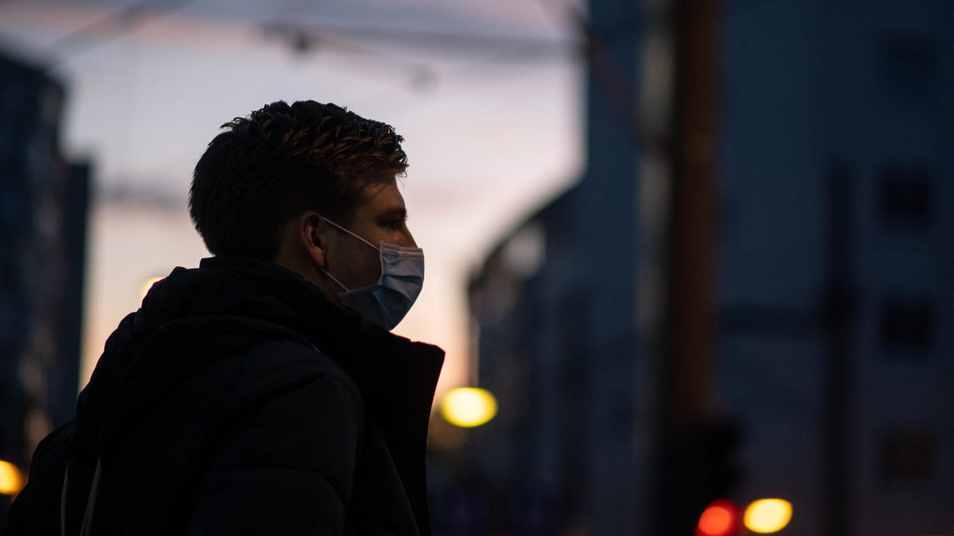 Ein Mann steht mit Mund- und Nasenmaske in der Dämmerung: In Stuttgart gilt nun eine Sperrstunde.